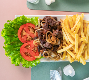 Prato com carne acebolada, rodelas de tomate, folhas de alface e porção de batatas fritas.